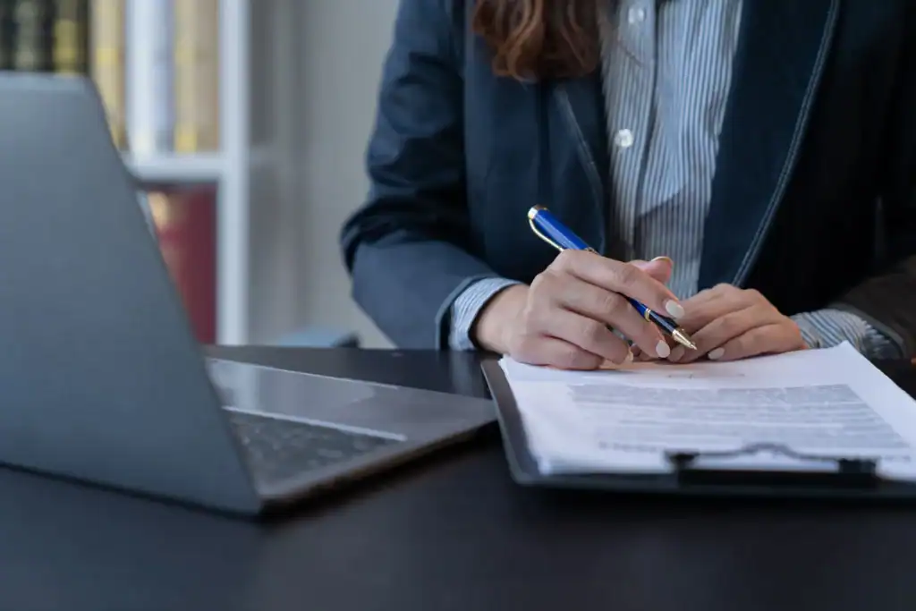 Gros plan sur une professionnelle examinant un document administratif. À côté d’un ordinateur portable, elle analyse un texte réglementaire et prépare des annotations afin d’évaluer ses impacts sur la gestion des ressources humaines.
